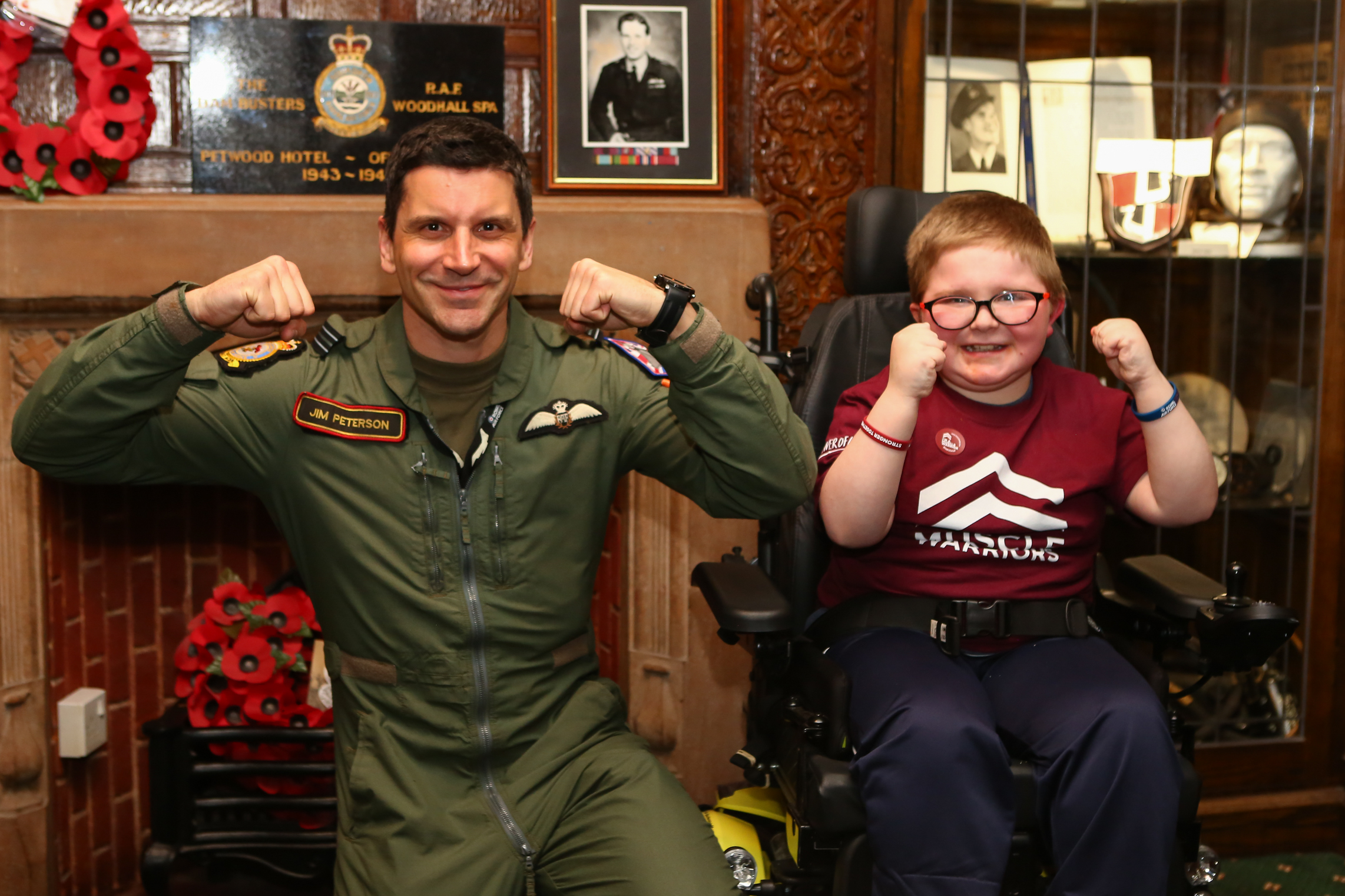 Fighter Pilot and a young wheelchair user doing a strongman pose and smiling at the camera